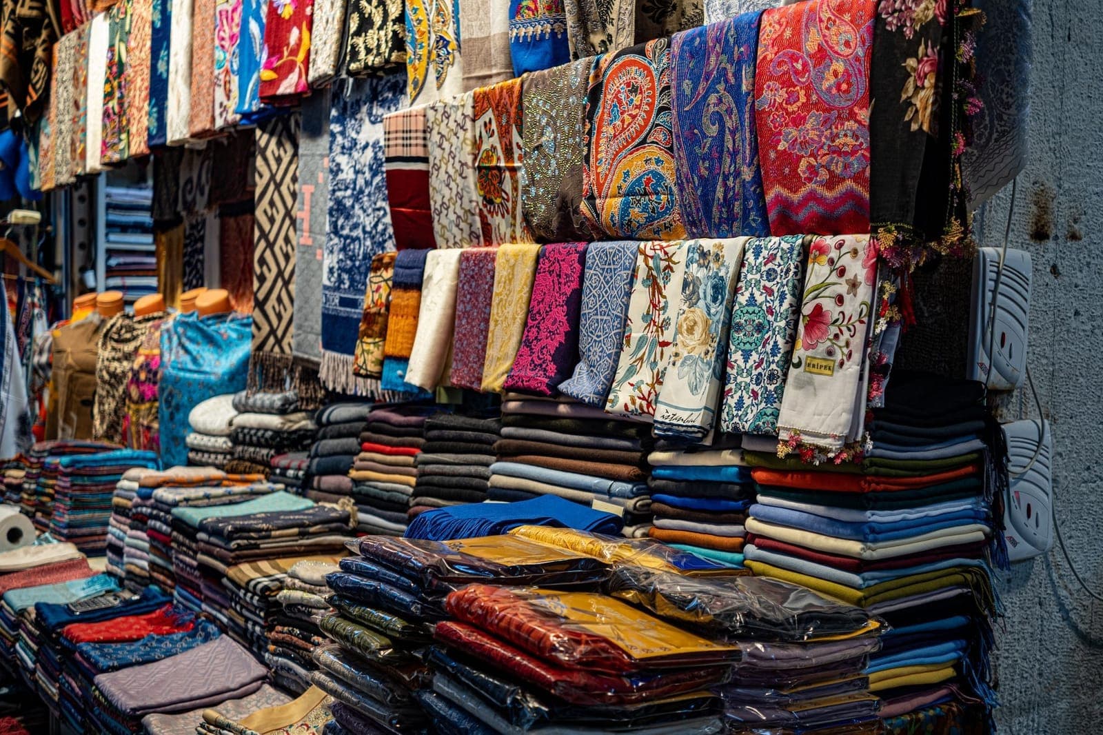 İstanbul'da bir pazarda toptan tezgâh düzeninde sıra sıra asılı ve katlanmış renkli başörtüleri ile şallar